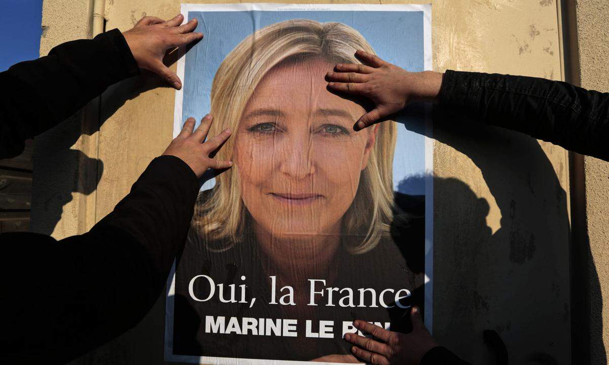 Supporters paste a poster of Marine Le Pen, France's National Front leader, on a wall before a political rally for local elections in Frejus