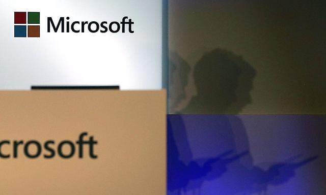 A shadow of a man using his mobile phone is cast near Microsoft logo at the 2014 Computex exhibition in Taipei