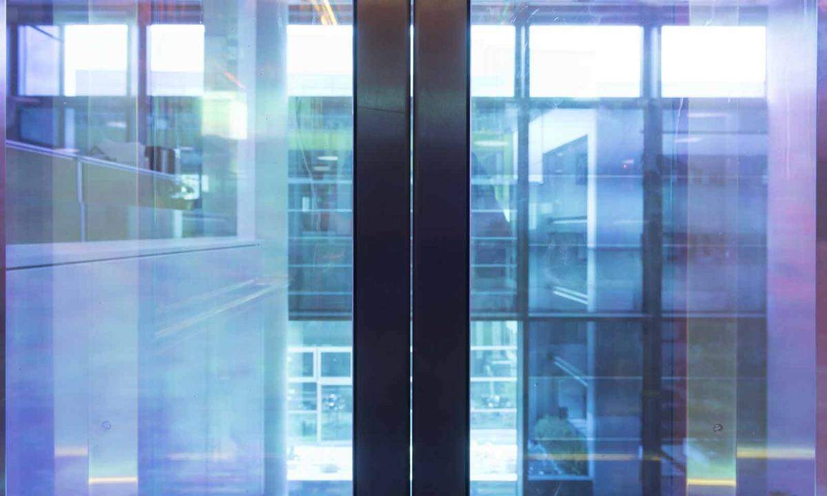 Der (Regenbogen-)Aufzug des Gebäudes ist mit einer Folie verkleidet, die nur bestimmte Wellenlängen durchlässt und andere reflektiert. Es geht nach oben.