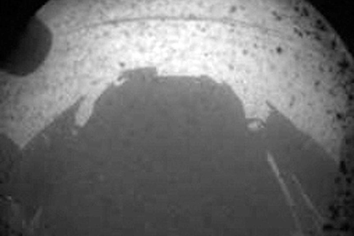 Das erste Bild folgte um 7:35 Uhr MEZ. Es gab noch nicht viel vom Landeplatz des Rovers im Gale Krater preis. Der Krater ist etwa 154 Kilometer breit und wird auf ein Alter von 3,5 bis 3,8 Milliarden Jahre geschätzt. Die Signallauftzeit zwischen Erde und Mars beträgt übrigens 13:48 Minuten für die rund 248 Millionen Kilometer zwischen den beiden Planeten.