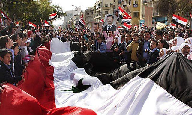 Pro-Syrian regime protesters, shout slogans and carry a giant Syrian flag during a demonstration agai