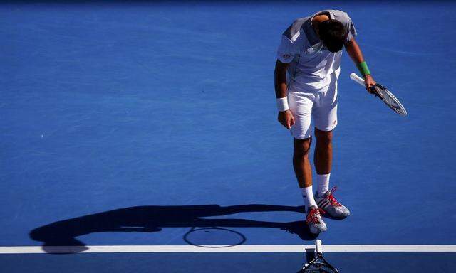 Novak Djokovic of Serbia picks up the racquet of Fabio Fognini of Italy after he threw it during their men's singles match at the Australian Open 2014 tennis tournament in Melbourne