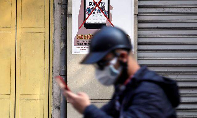 A man uses a smartphone as he walks past a poster warning against spreading 'fake news' on the coronavirus in Hanoi