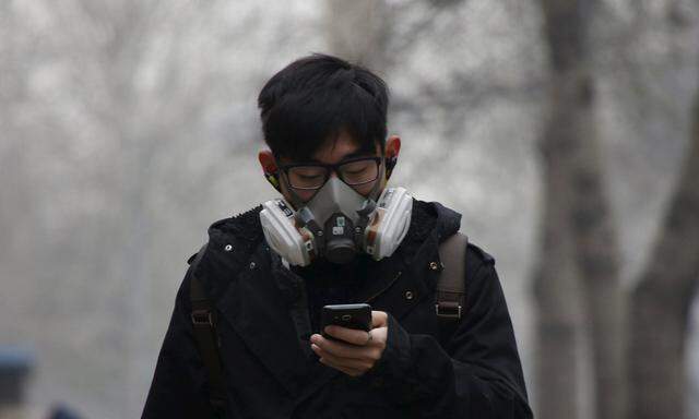 A man wearing a mask uses his mobile phone amid heavy smog after the city issued its first ever ´red alert´ for air pollution, in Beijing, China