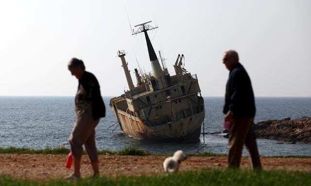 Tourists walk near a shipwreck in the coastal village of Pegeia