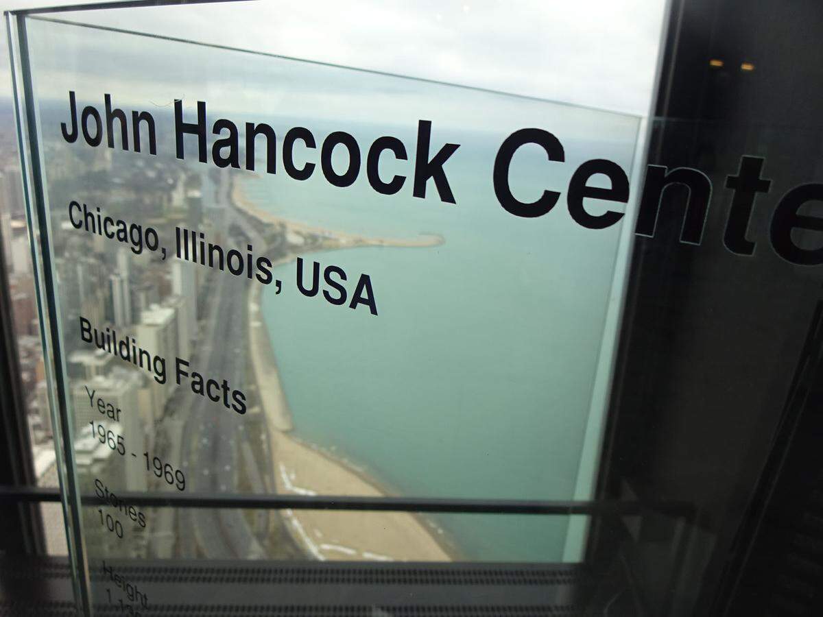 Wir befinden uns auf der Aussichtsplattform des John Hancock Center (erbaut 1969, benannt nach dem ersten Unterzeichner der Unabhängigkeitserklärung, 1737-1793), im 94. Stock, ungefähr 300 Meter über dem Boden. Das ehemals höchsten Gebäude Chicagos, damals auch zweithöchstes der Welt, wurde jüngst in 360 Chicago umbenannt, aber keiner sagt so.