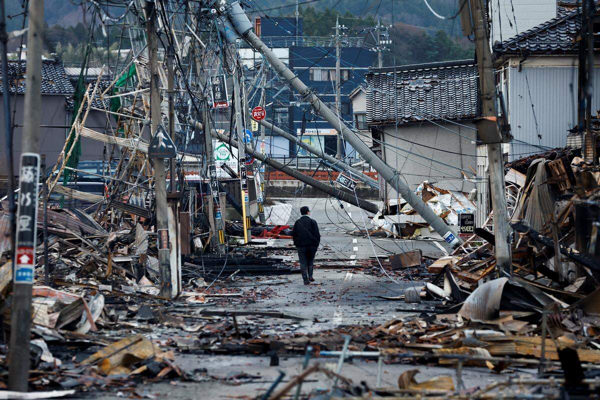 4. Jänner. Das Leben nach dem Erdbeben. Ein Mann macht sich auf den Weg entlang der gänzlich zerstörten Asaichi-dori-Straße in Wajima, Japan.
