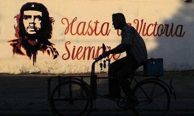 A graffiti of revolutionary character Ernesto 'Che' Guevara is seen on a wall as a men rides past on his tricycle in Havana