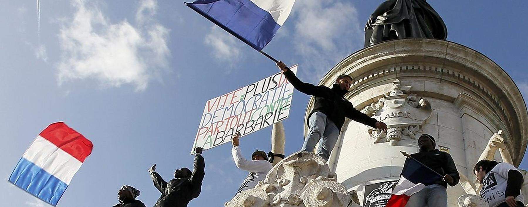 People holding a poster reading 'Quick more democracy everywhere against barbarism' take part in a solidarity march (Marche Republicaine) in the streets of Paris