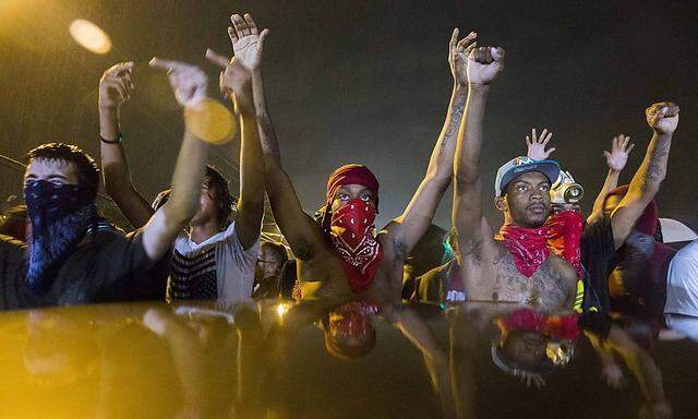 Protesters gesture as they stand in the street in defiance of a midnight curfew in Ferguson, Missouri