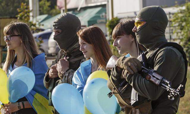 People draped with national flags on their shoulders pose for a photo with armed Ukranian soldiers during a pro-Ukranian meeting in Mariupol