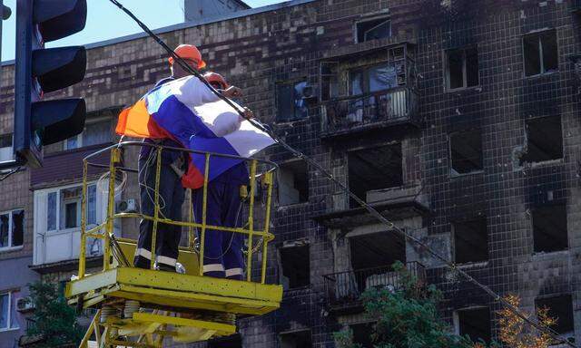 Eine russische Flagge wird vor einem beschädigten Gebäude angebracht. 
