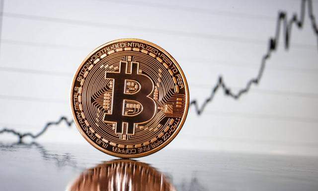 Symbolfoto zum Thema Bitcoins virtuelle Waehrung Eine Bitcoin Muenze steht vor einem aufsteigende