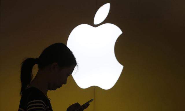 A woman looks at the screen of her mobile phone in front of an Apple logo outside an Apple store in downtown Shanghai