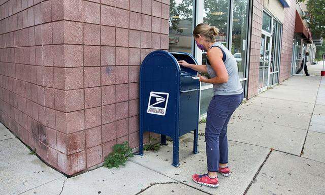 An individual deposits letters into a U.S. Postal Service (USPS) collection mailbox in Philadelphia