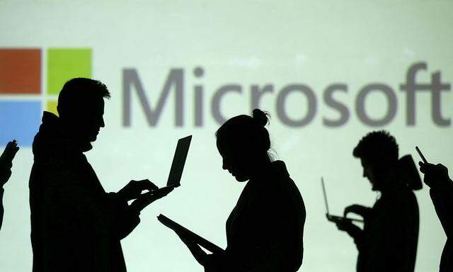 FILE PHOTO: Silhouettes of laptop and mobile device users are seen next to a screen projection of Microsoft logo in this picture illustration