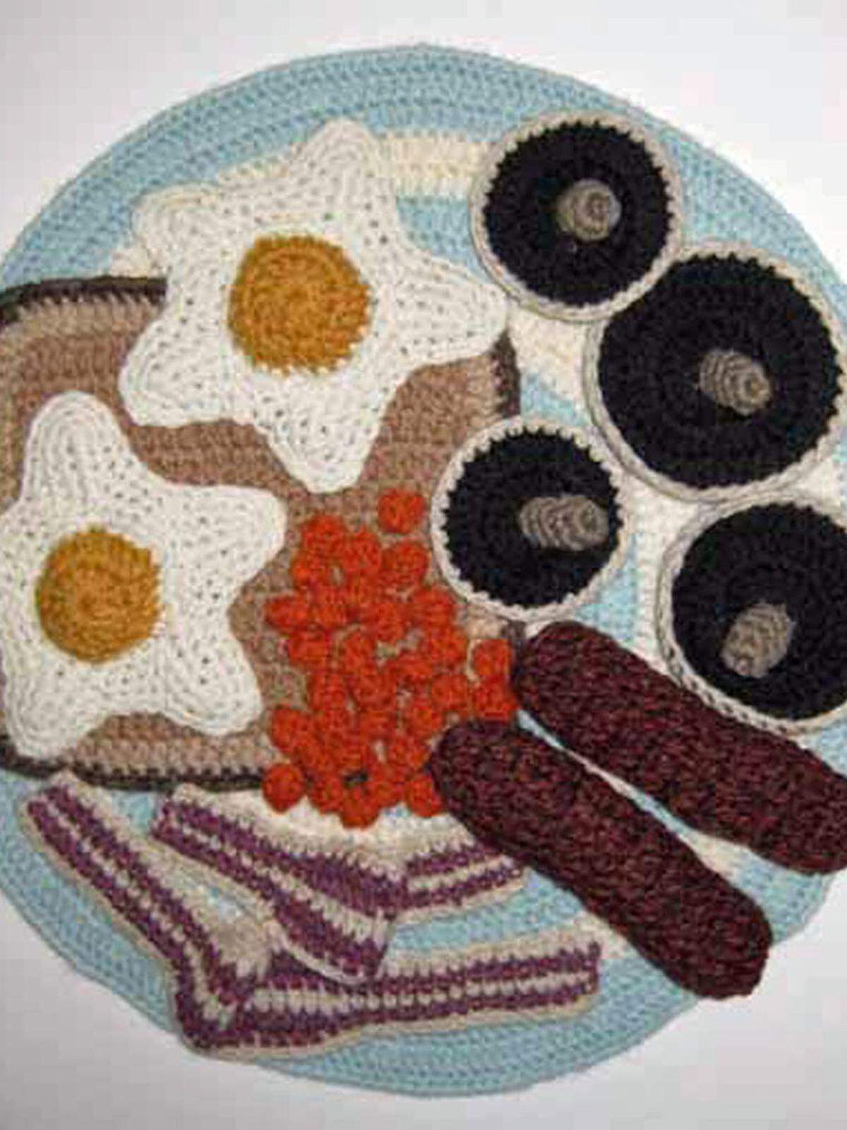 Die britische Künstlerin bereitet maschenweise Snacks zu: Garnelentoast mit Gurke, runde Cracker mit Schinken, Oliven und Ei, süße Obsttörtchen oder „Sewshi“. Gegen Kater hält sie ein deftiges englisches Frühstück bereit, mit gegrillten Champignons, Wurst, Eiern und Bohnen, für Luxusgeschöpfe fertigt sie Kaviardosen.  Gehäkelte Wolle, 2008, 33,5 x 33,5 cm.