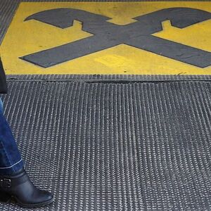 A woman walks by a Raiffeisen logo painted on the ground in front of an office building in Vienna