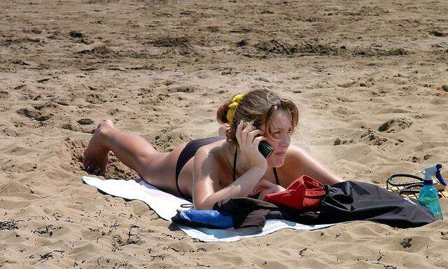 Frau am Sandstrand telefoniert mit einem Handy im Ausland