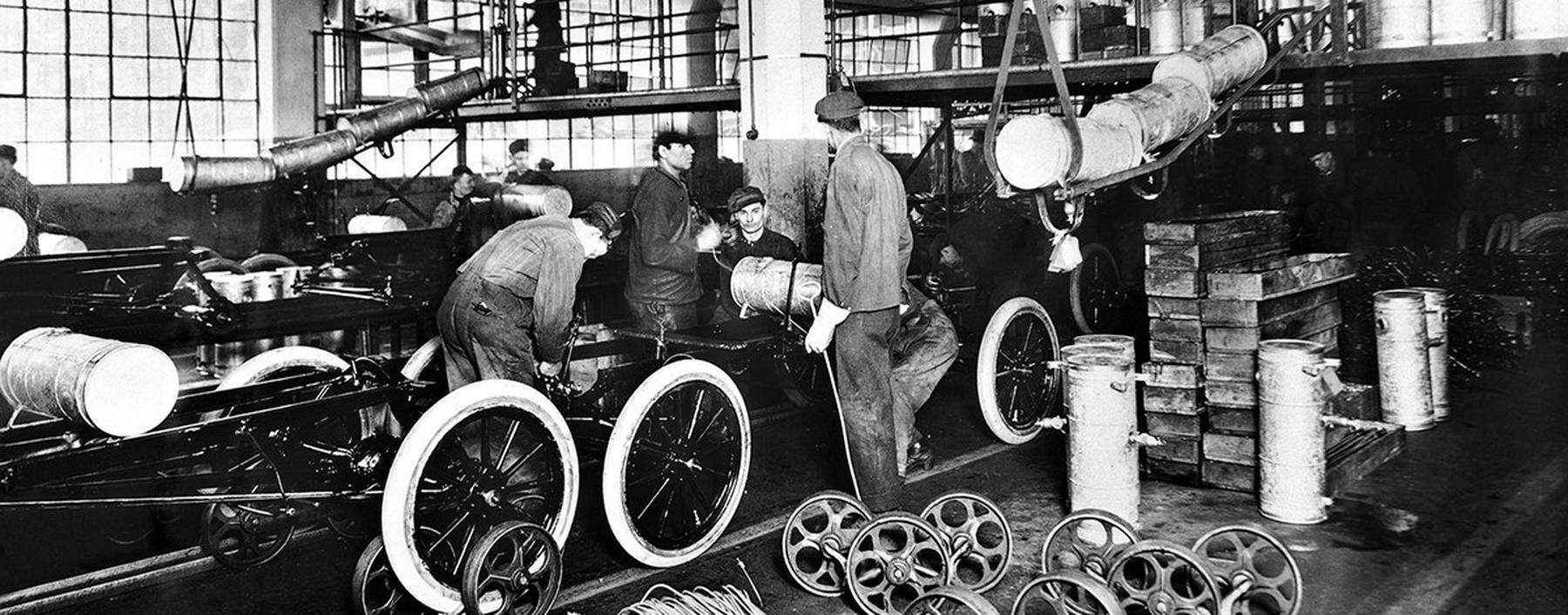 Aufnahme mit Arbeitern am Model T aus dem Jahr 1913: Henry Ford führt in seinem Werk in Detroit die Fließbandproduktion ein: „Die Geburtsstunde der modernen Autoindustrie.“ 