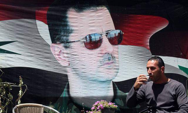 A Syrian man takes a drink beside a poster of Syria s President Bashar al Assad in Damascus capita