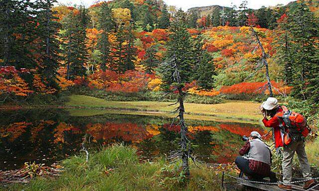 Hikers take photos of autumn leaves that is reflected in the surface of Takimi Lake on Taisetsu Mount