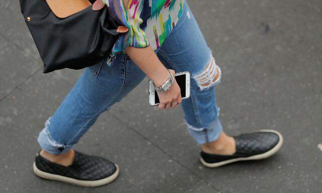 A woman holds an Apple iPhone as she walks on a street in New York