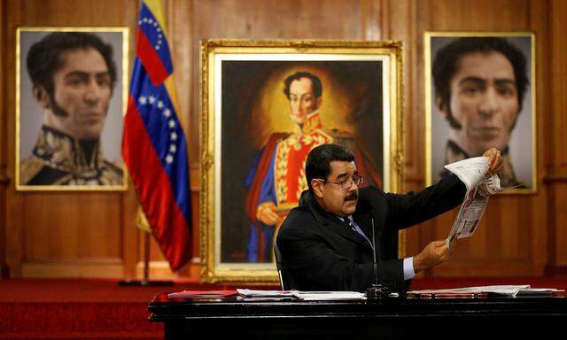 Venezuela's President Nicolas Maduro holds a copy of a newspaper as he speaks in front of images of South American hero Simon Bolivar during a news conference at Miraflores Palace in Caracas