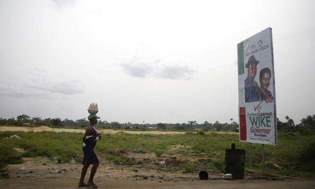 A woman selling groundnut, walks past a billboard campaigning for Nyesom Wike, People's Democratic Party candidate in River state, along a road in Mbiama village