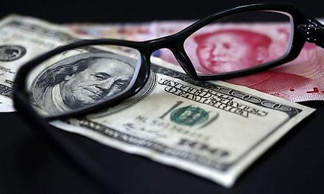 A U.S. dollar note and a Chinese yuan banknote are seen through a pair of spectacles in this picture 