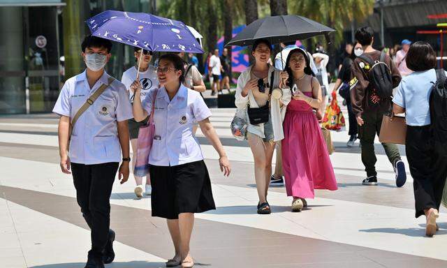 Fußgänger schützen sich mit Sonnenschirmen vor der Hitze in Bangkok.