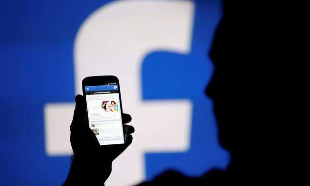 FILE PHOTO: A man is silhouetted against a video screen with a Facebook logo as he poses with a smartphone in this photo illustration