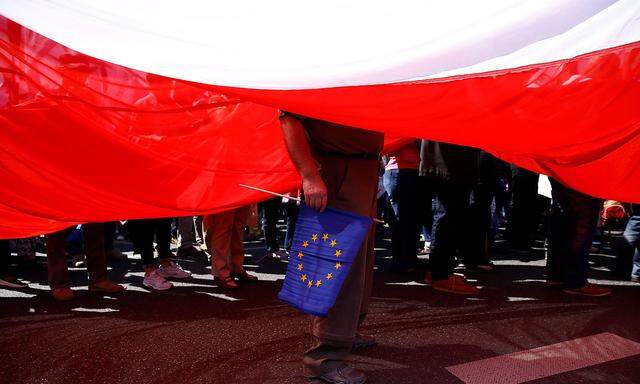 A man holds EU flag as he stands under a giant Polish flag during anti-government demonstration organized by main opposition parties in Warsaw