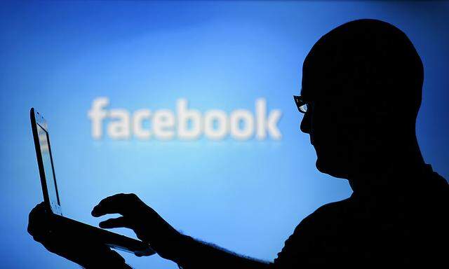 A man is silhouetted against a video screen with an Facebook logo as he poses with an Dell laptop in this photo illustration taken in the central Bosnian town of Zenica