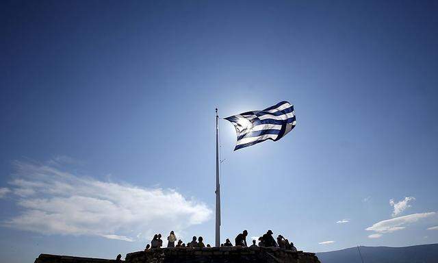 A Greek flag flutters as tourists visit the Acropolis hill archaeological site in Athens