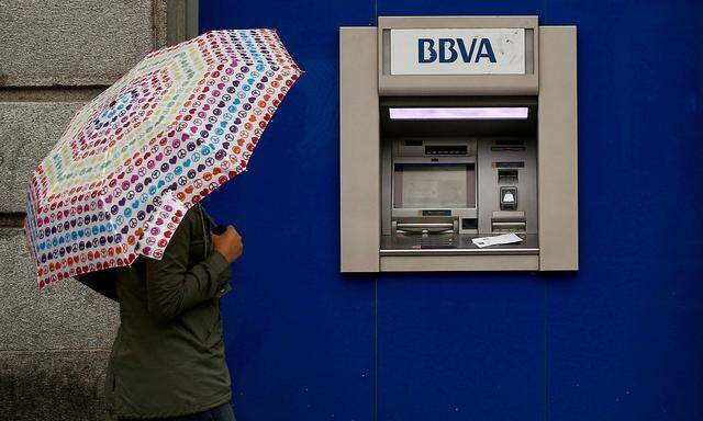 FILE PHOTO: A woman with an umbrella walks past a BBVA bank branch in central Madrid, Spain