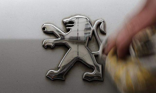 A man cleans a company logo on a Peugeot car parked in Paris