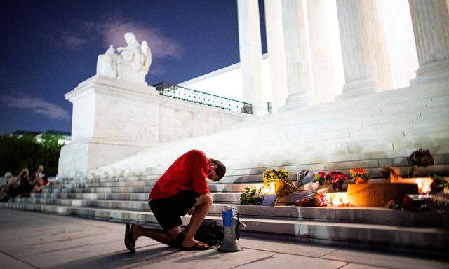 A man kneels as he brings a megaphone to a vigil on the steps of the U.S. Supreme Court following the death of U.S. Supreme Court Justice Ruth Bader Ginsburg, in Washington