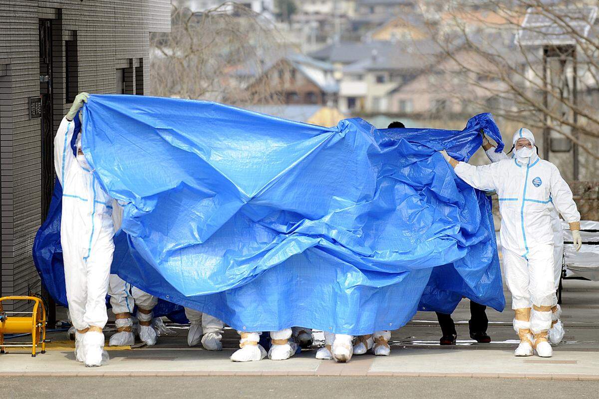 Soldaten in Spezialanzügen überstellen Arbeiter des AKW Fukushima, die radioaktiver Strahlung ausgesetzt waren. (25. März)