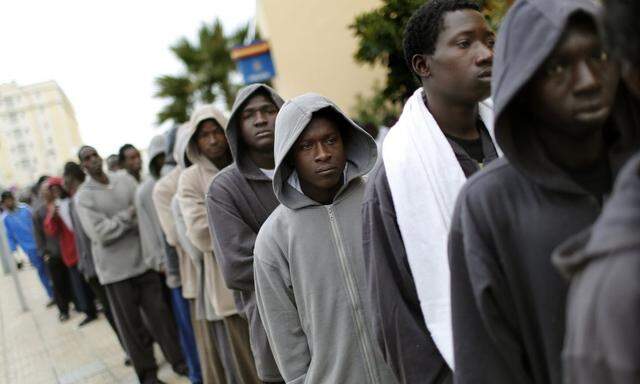 African migrants stand in a queue as they wait to receive temporary identity cards for their stay at a refugee centre, outside a police station in Melilla