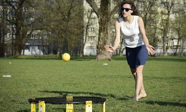 Eine junge Frau spielt Roundnet im Park, auch Spikeball genannt. 