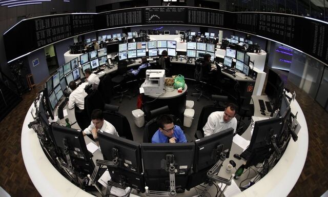 Traders are pictured at their desks in front of the DAX board at the Frankfurt stock exchange