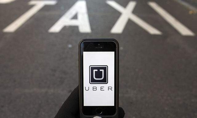 Photo illustration of logo of car-sharing service app Uber on a smartphone over a reserved lane for taxis in a street in Madrid