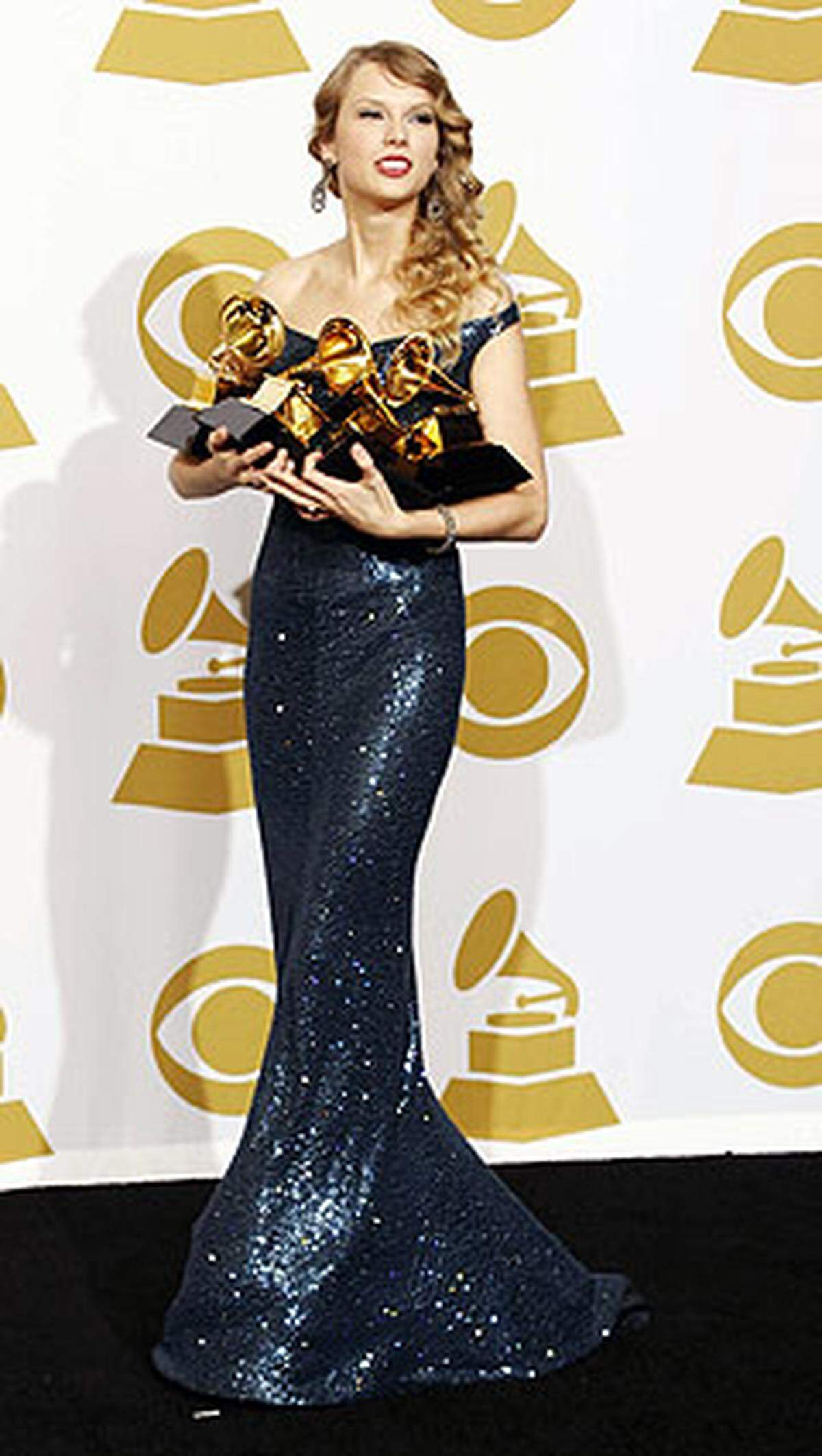 20 Jahre und schon vier Grammys im Arm (einen hat sie im Blitzlichtgewitter fallen lassen) - Taylor Swift leuchtet in einem nachtblauen Kaufman Franco-Kleid, trägt Geschmeide von Lorraine Schwartz und Schuhe von Christian Louboutin.