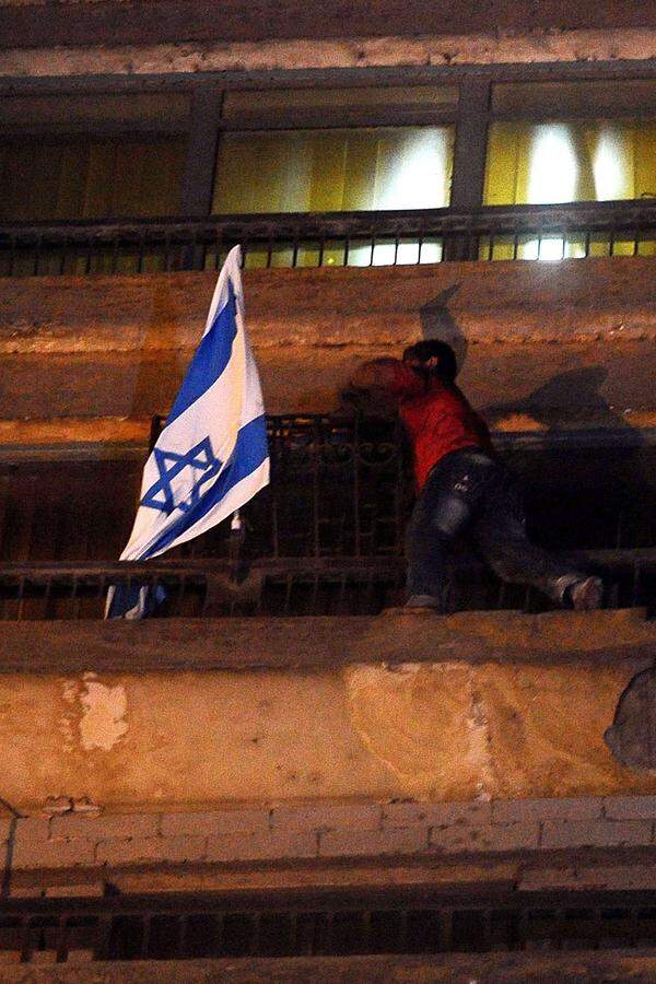 Ein Mann klettert die Fassade hoch und entfernt Israels Fahne von dem Gebäude. Unter dem Jubel der Demonstranten wirft er sie auf die Straße.