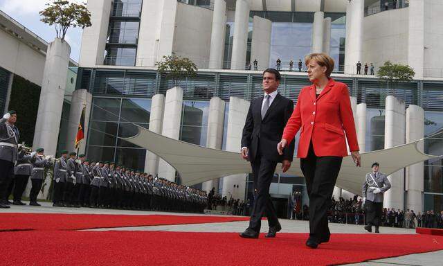 French Prime Minister Valls and German Chancellor Merkel review a guard of honour during a welcome ceremony at the Chancellery in in Berlin