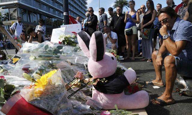 People gather near flowers, candles and a stuffed toy as they pay tribute near the scene where a truck ran into a crowd at high speed killing scores and injuring more who were celebrating the Bastille Day national holiday in Nice