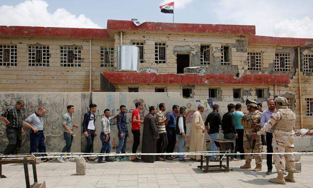 Iraqi people stand in a queue to cast their vote at a polling station during the parliamentary election in Mosul