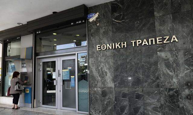 A woman makes a transaction at an ATM machine outside a National bank branch in Athens