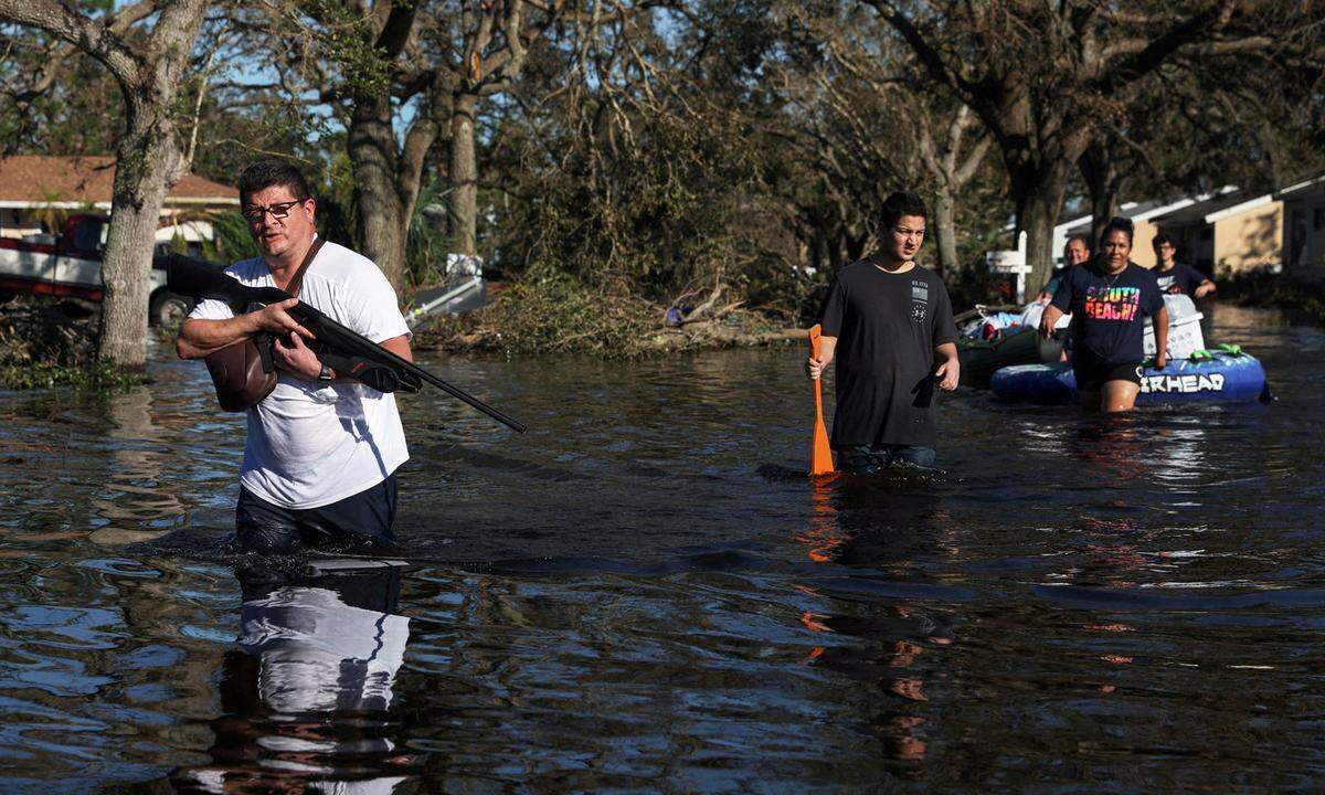 30. September 2022. Ein Mann mit Gewehr geht mit einer Familie durch eine überflutete Straße, nachdem Hurrikan "Ian" große Zerstörungen in der Stadt North Port, Florida, angerichtet hatte.